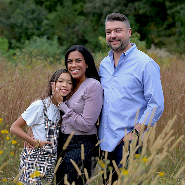 Kevin with wife and daughter smiling in a field